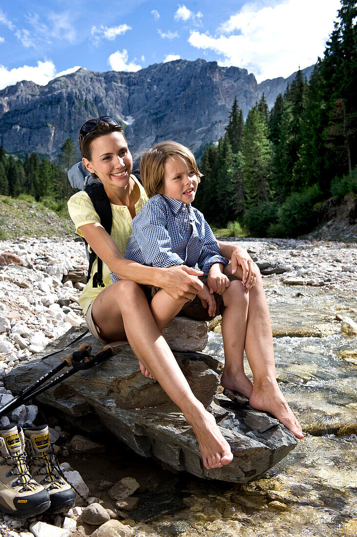 A woman and a boy sitting on a rock at the riverbank, South Tyrol, Italy, Europe