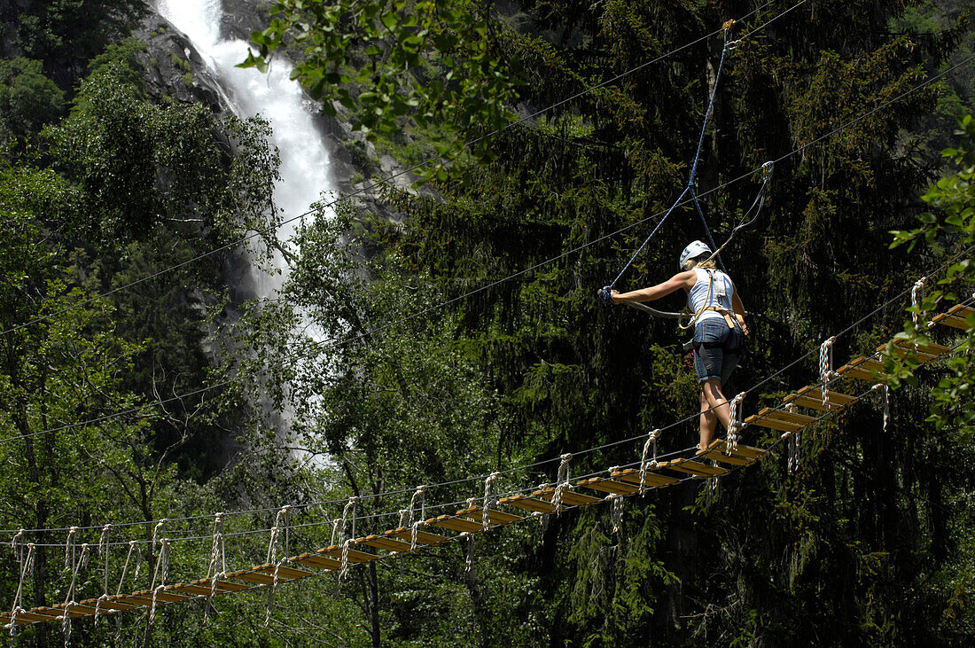 Eine Person auf einer Hängebrücke in einem Klettergarten, Partschinser Wasserfall im Hintergrund, Vinschgau, Alto Adige, Südtirol, Italien, Europa