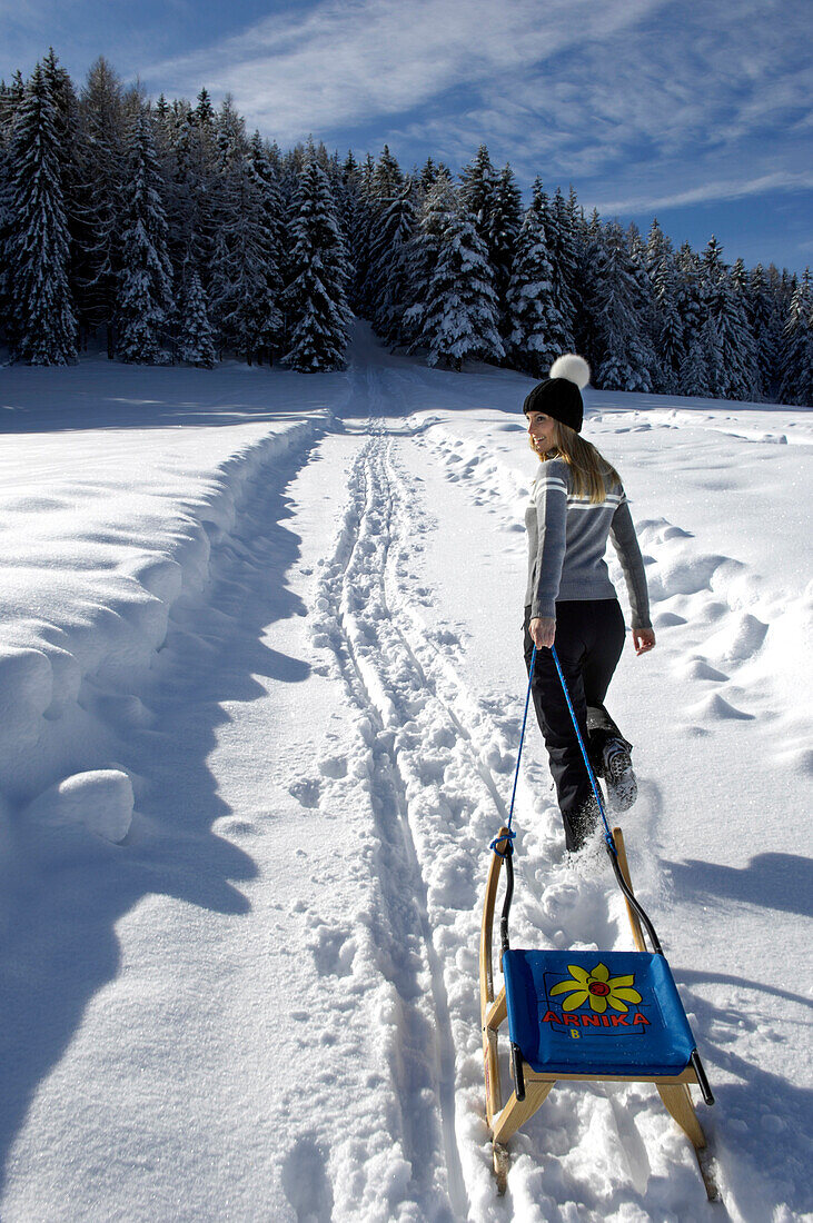 Junge Frau mit Schlitten in verschneiter Winterlandschaft, Alto Adige, Südtirol, Italien, Europa
