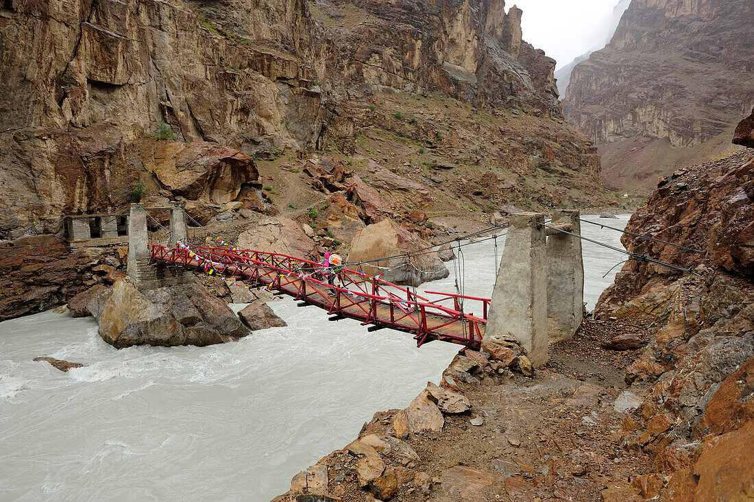 Woman crossing river on suspension bridge near Phuktal monastery, Phuktal, Zanskar Range Traverse, Zanskar Range, Zanskar, Ladakh, Jammu and Kashmir, India