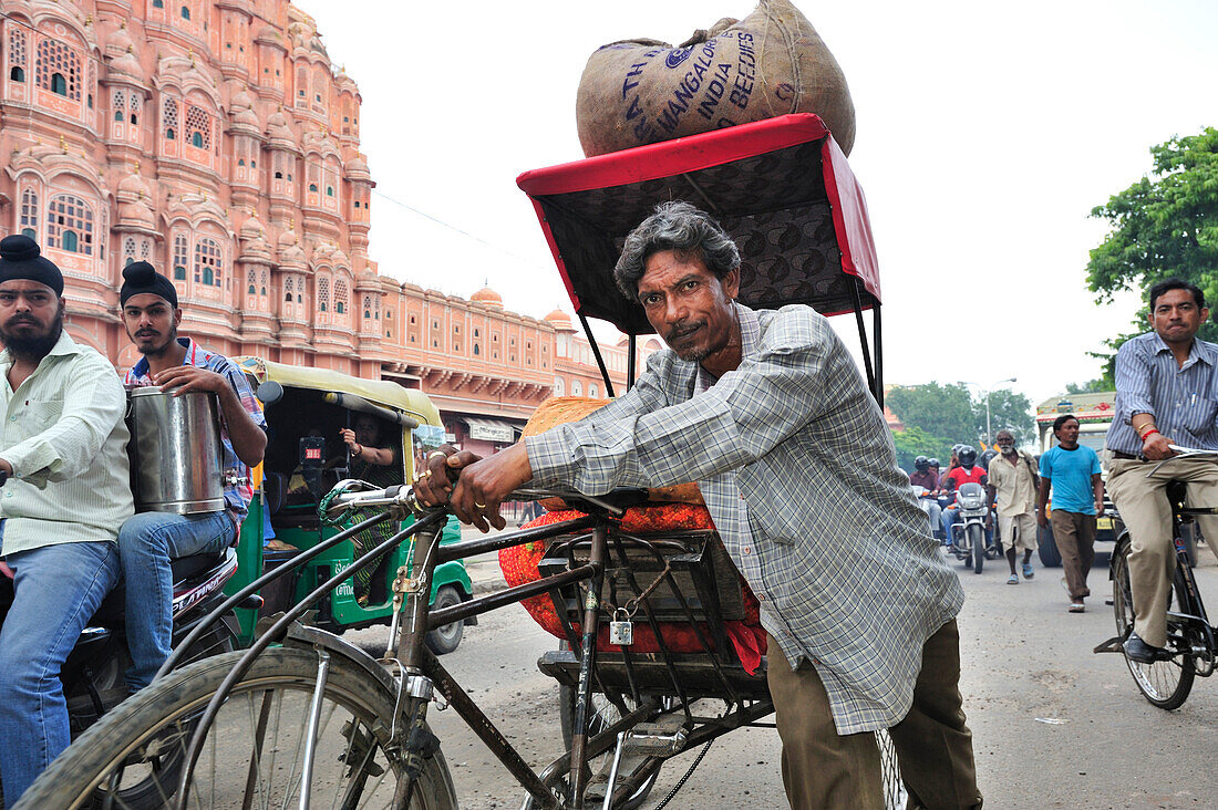 Man pushing loaded rickshaw in front of palace of winds, palace of winds, Hawa Mahal, Jaipur, Rajasthan, India