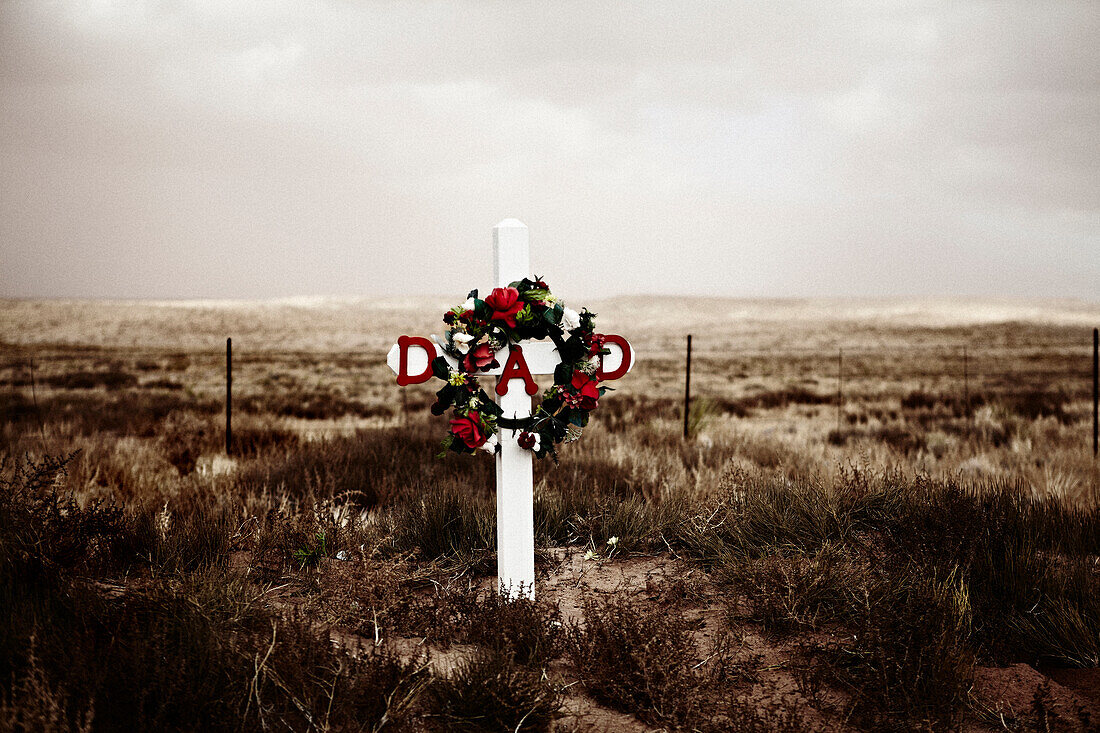 Cross and Wreath of Flowers at Gravesite in Arid Field, Arizona, USA