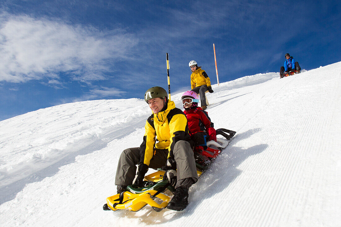 Zwei Männer, eine Frau und ein kleines Kind, Mädchen beim Schlittenfahren auf der Schlittelbahn im Wintersportgebiet Stoos mit dem modernen Schlitteln Scorpion Racer, Kanton Schwyz, Schweiz