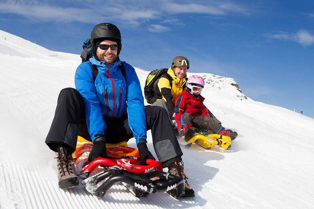 Zwei Männer und ein Mädchen beim Schlittenfahren auf der Schlittelbahn im Wintersportgebiet Stoos, Mit dem modernen Schlitten Scorpion Racer, Kanton Schwyz, Schweiz