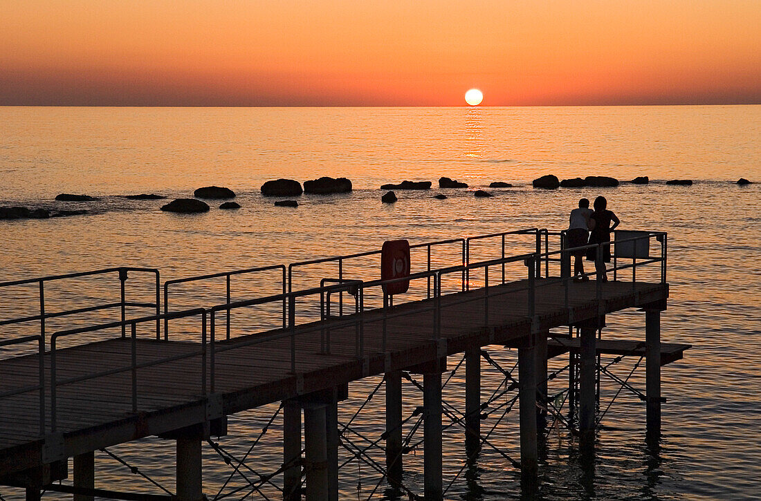 A silhouetted couple watch the sun setting out at sea, Cyprus