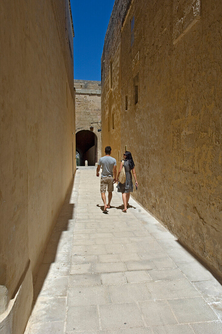 Couple walking along narrow passage, rear view, Midina, Malta