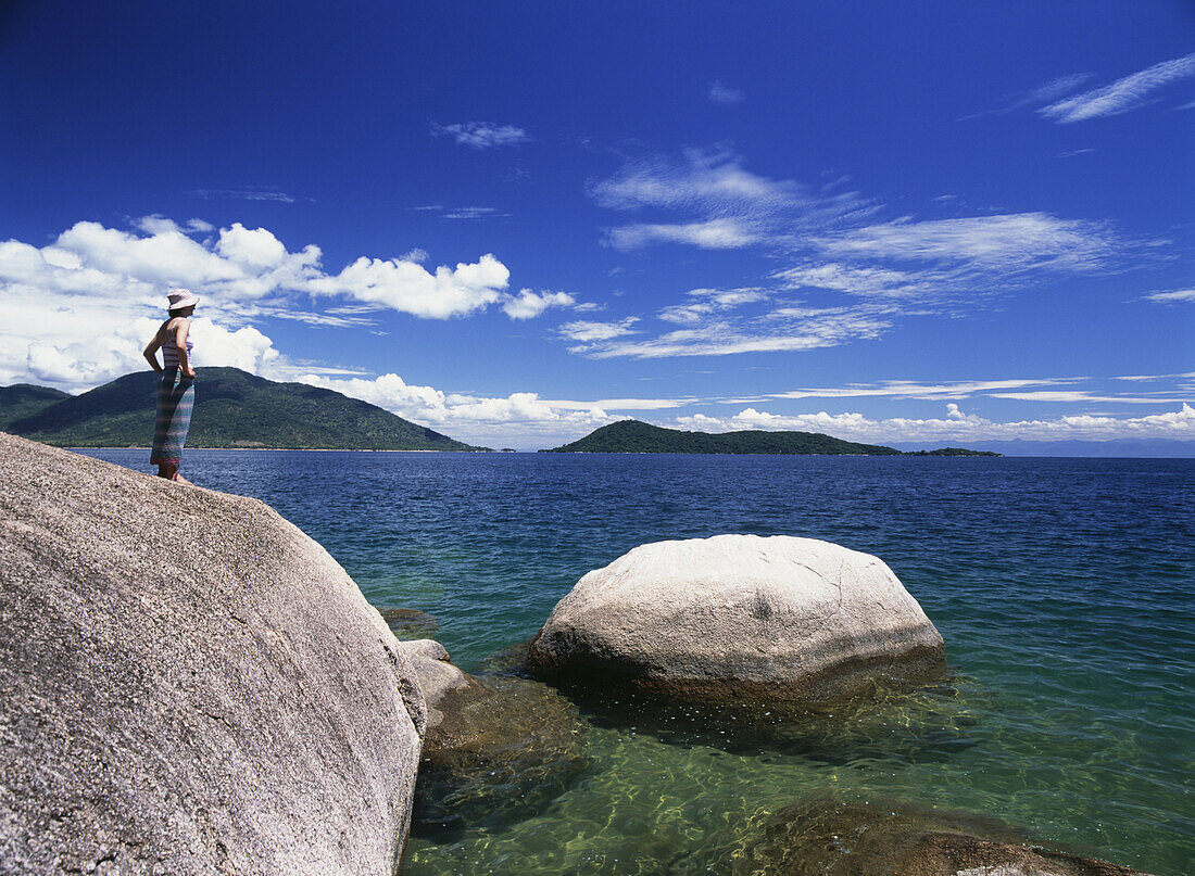 Woman looking out from large rocks on the island of Domwe, Lake Malawi, Malawi