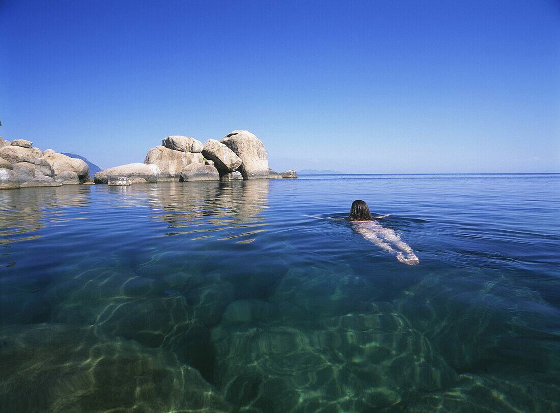 Woman swimming out to rocks off Mumbo Island, Lake Malawi, Malawi