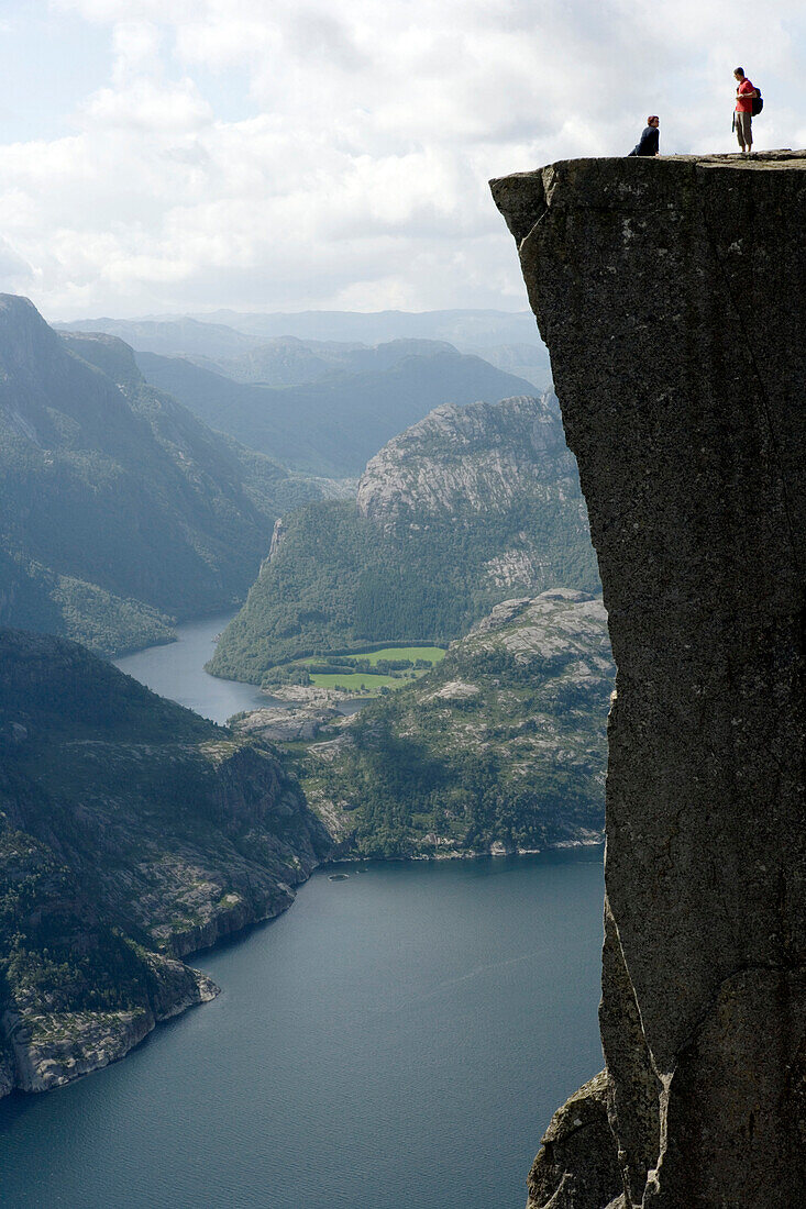 Two people standing on edge of Pulpit Rock, Preikestolen, above Lysefjorden, Norway