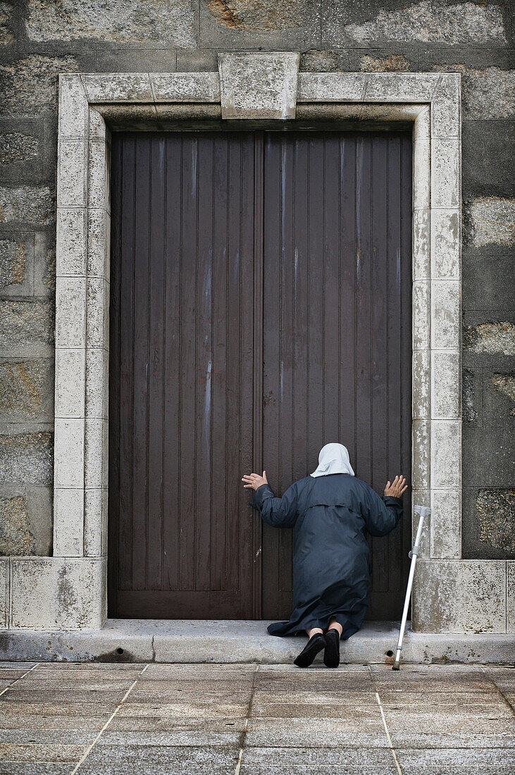 An old lady kneels in worship at the door of the Church, Muxia, Galicia, Spain
