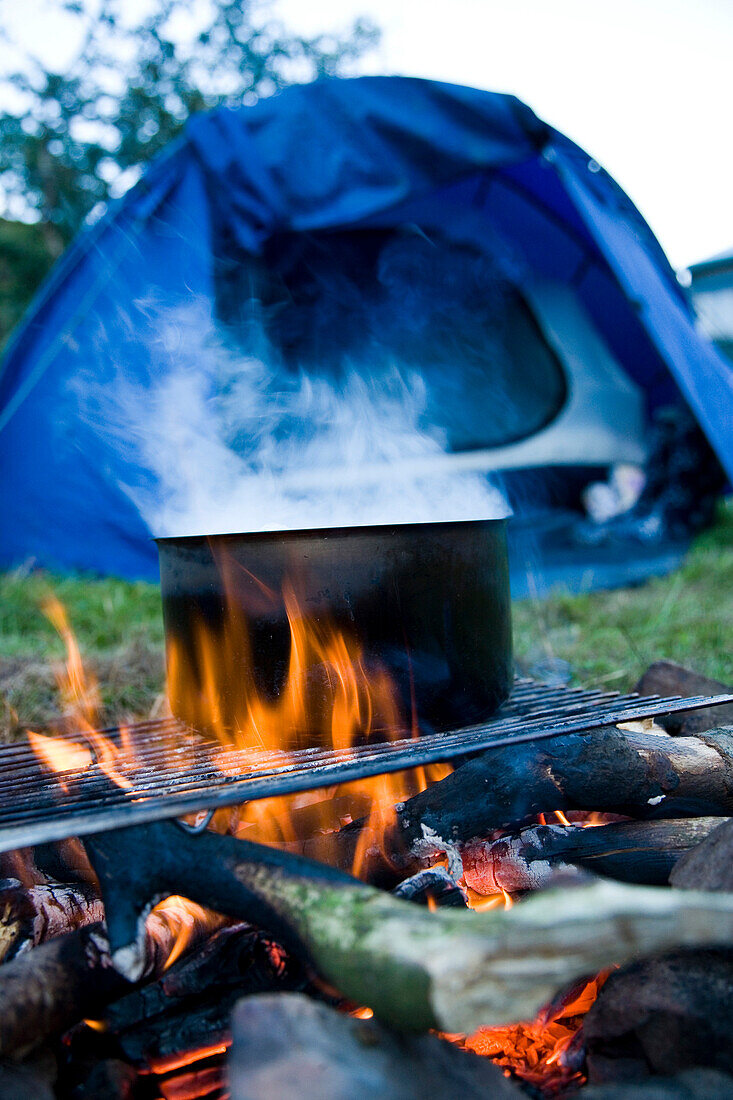 Steaming pot on campfire with tent in background, North Devon, Exmoor, England