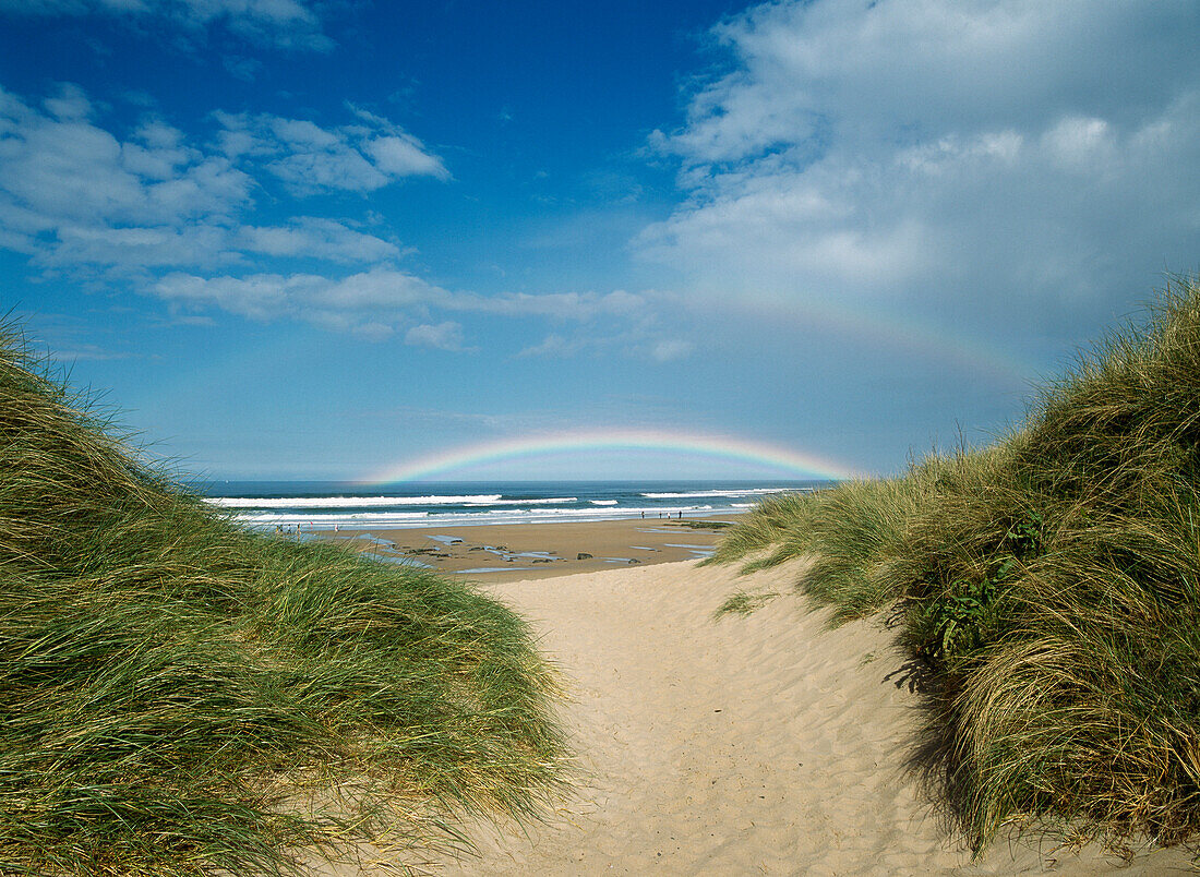 Looking through gap in dunes to double rainbow, Embleton Bay beach near Dunstanburgh Castle, Northumberland, England