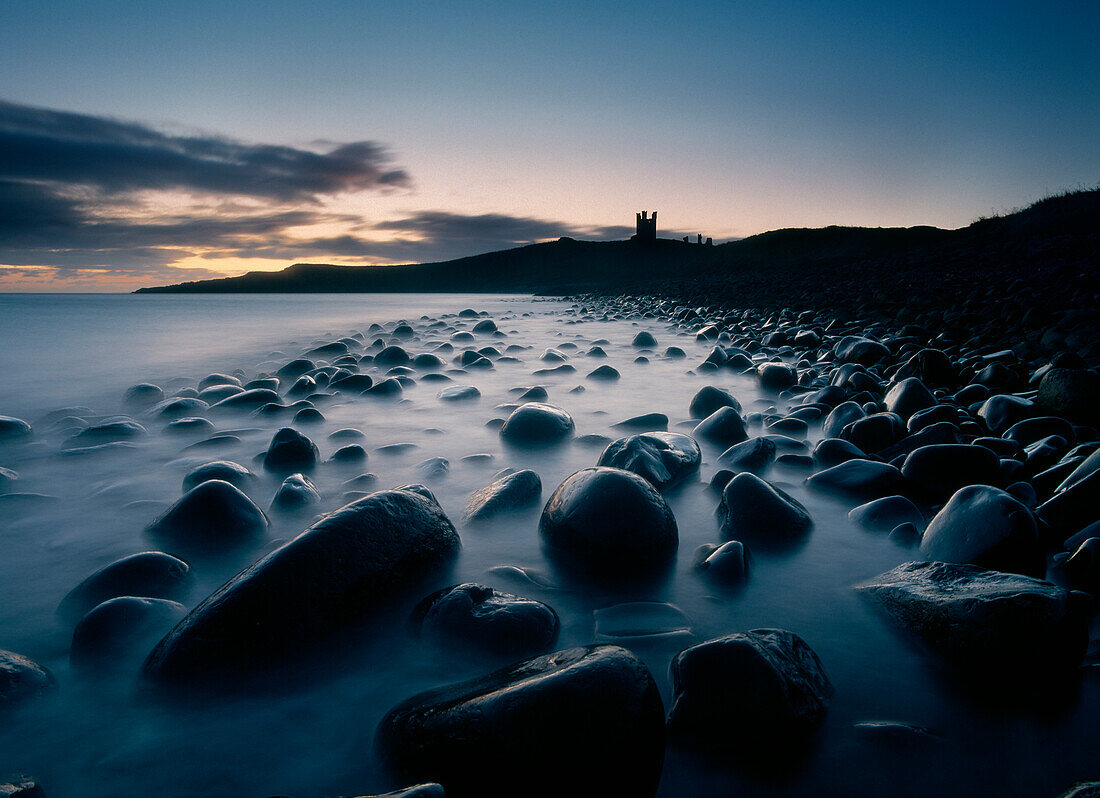 Large boulders on beach near Dunstanburgh Castle at dawn, Northumberland, England