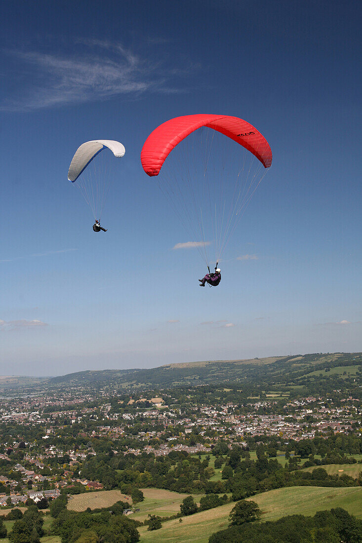 Two people paragliding over Cotswolds escarpment above National Trail, Cheltenham, Gloucestershire, England, UK