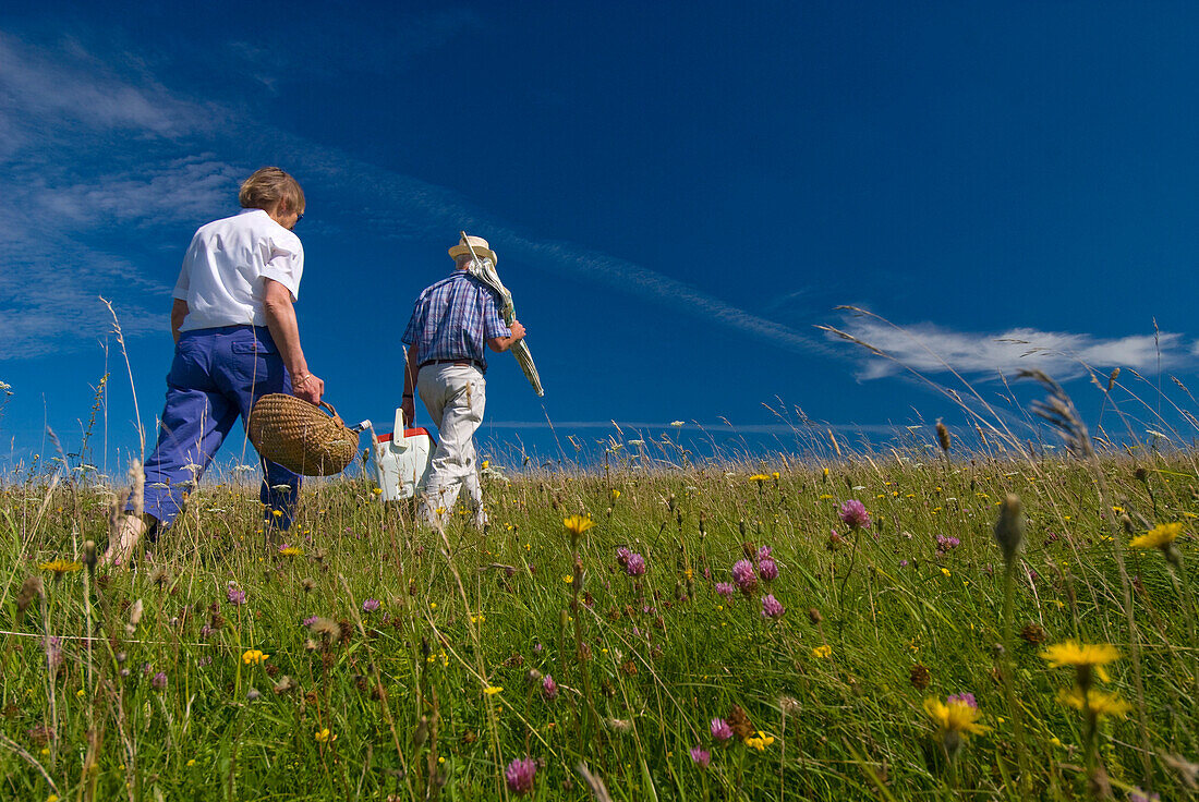 Couple carrying picnic baskets in meadow on the South Downs, West Sussex, England
