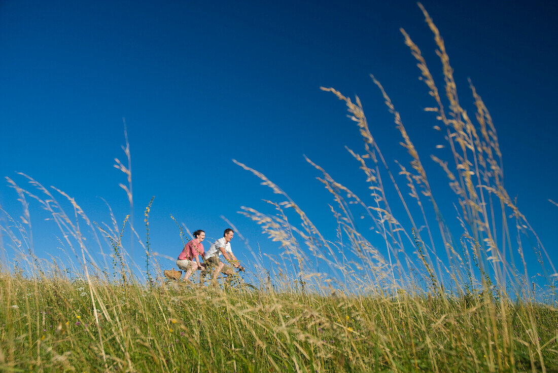 Couple going through meadow on tandem bicycle on the South Downs, Low Angle View, West Sussex, England