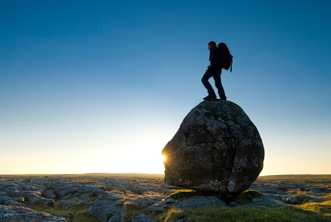 Hiker standing on head-shaped boulder, Twisleton Scars near Ingleton, Yorkshire Dales National Park, North Yorkshire, England