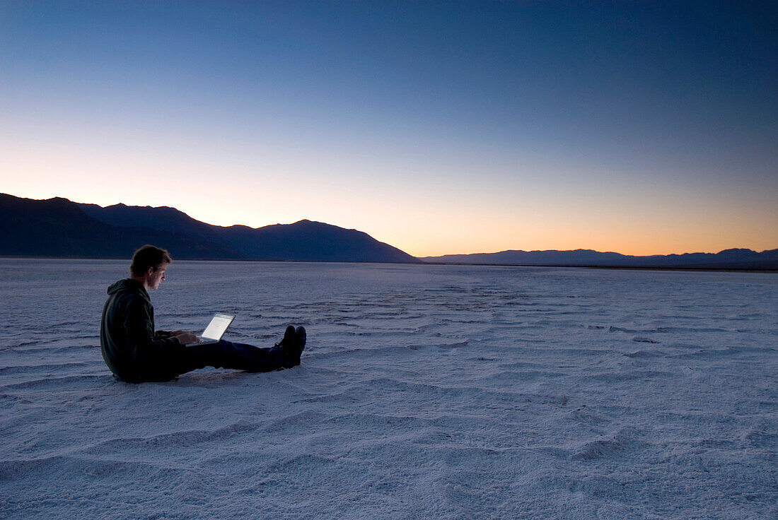 Man using laptop on the salt pans at dawn, Death Valley, California