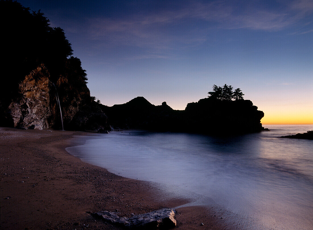 Looking out to sea at dusk from small beach with McWay Waterfall at end, Julia Pfeiffer State Park, Big Sur, California
