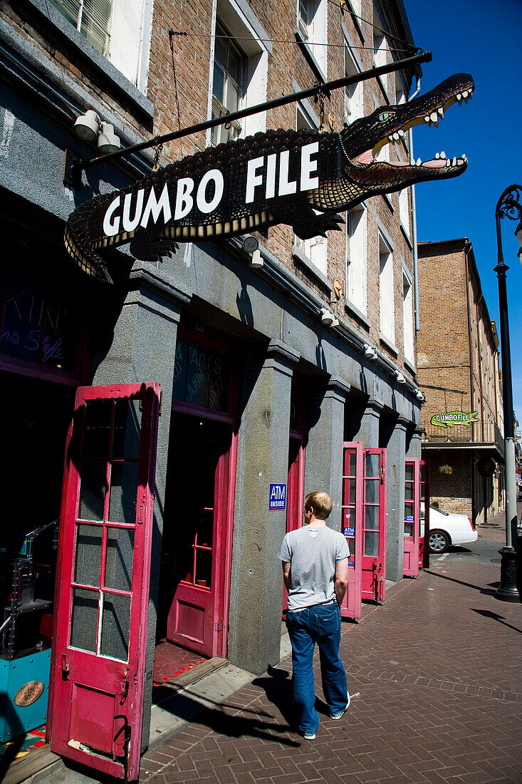 A man walks past a crocodile shaped sign for Gumbofile, a cafe bar, in the French Quarter, New Orleans, Louisiana, USA