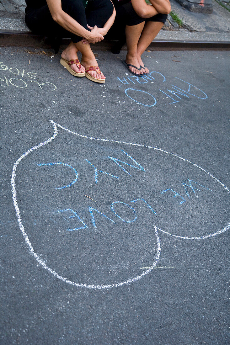 Two women sitting on curb by chalk drawing, low section, New York City, New York State, USA