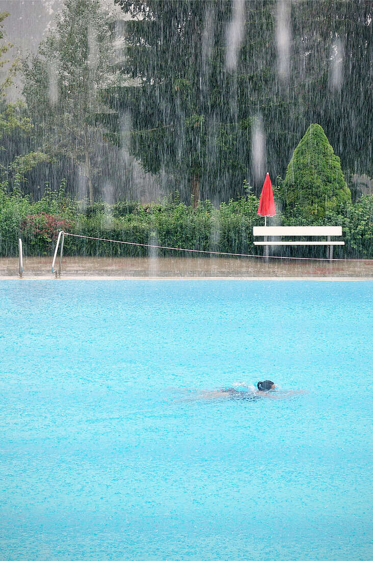 Badegast schwimmt während starkem Regenfall, Freibad Spiesel, Aalen, Schwäbische Alb, Baden-Württemberg, Deutschland
