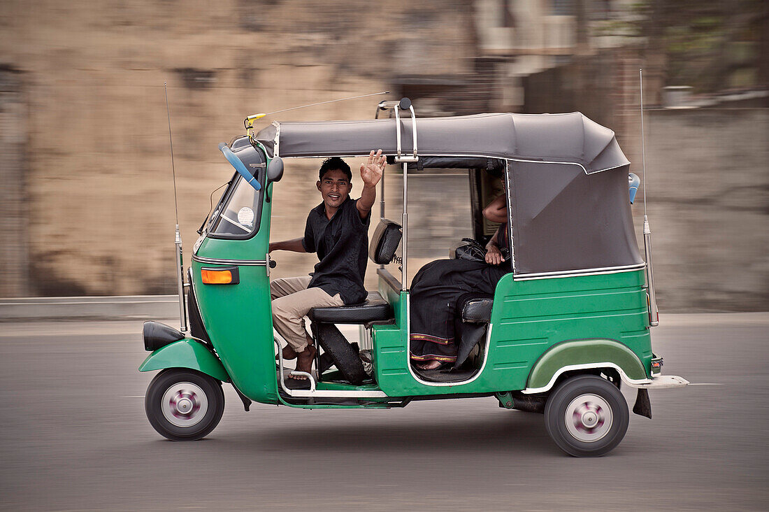 Einheimischer Tuk Tuk Fahrer winkt im vorbeifahren aus seinem motorisierten Dreirad, Hauptstadt Colombo, Sri Lanka