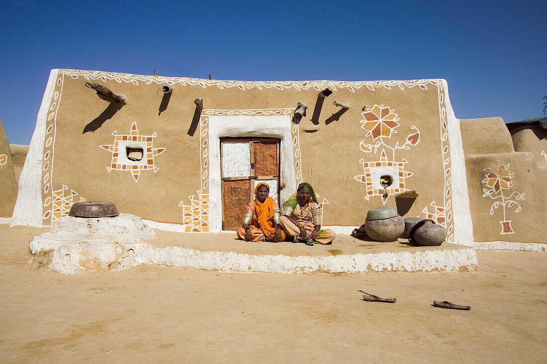 Two women siting in front of decorated mud hut, Jaisalmer, Rajasthan, India