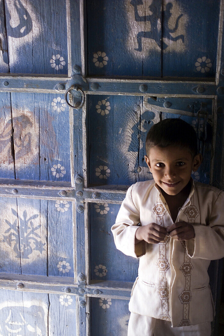 A young boy standing in front of a decorated julaha door in Jodpur, Rajasthan, India