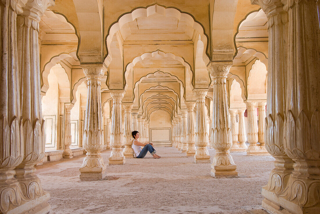 Tourist sitting in columned hallway in the  Amber Fort, Jaipur, Rajasthan, India