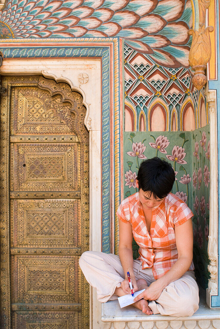 Woman writing postcard in decorated entrance area of the City Palace, Jaipur, Rajasthan, India