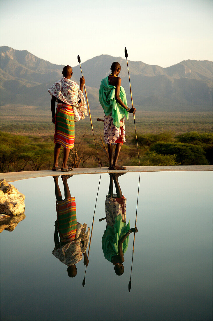Two Masai tribesmen standing at the edge of infinity pool, Namunyak, Matthews Mountains, Kenya