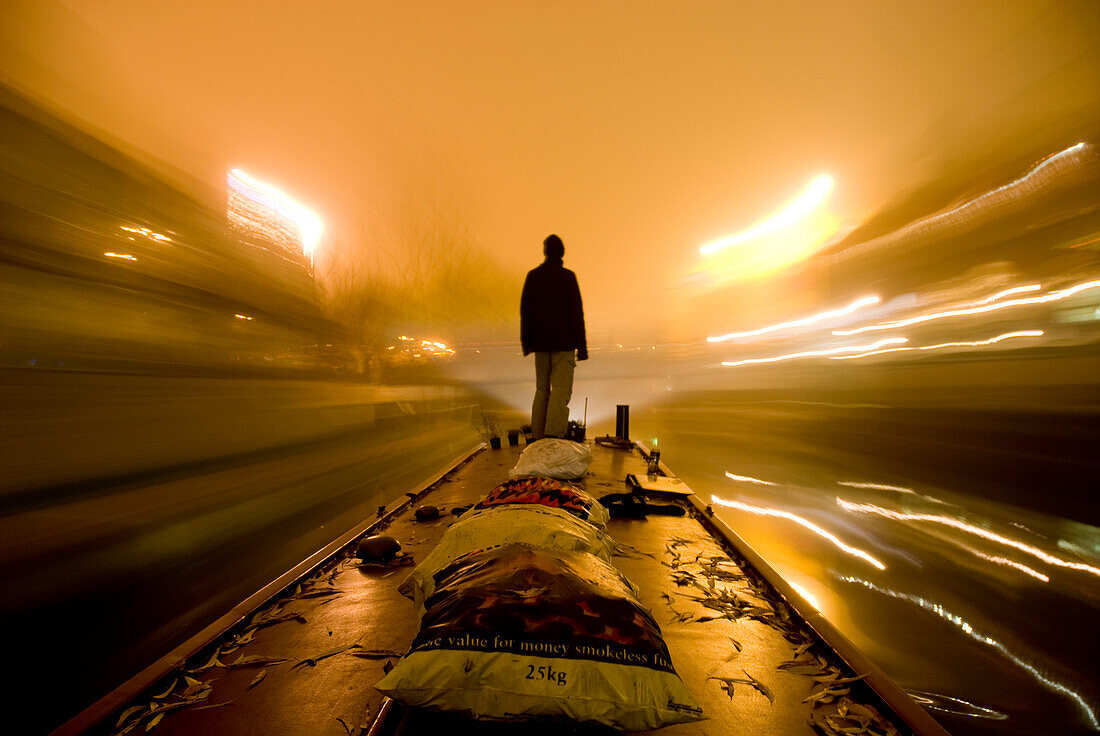Man standing on barge going along the canal on a foggy night, London, England