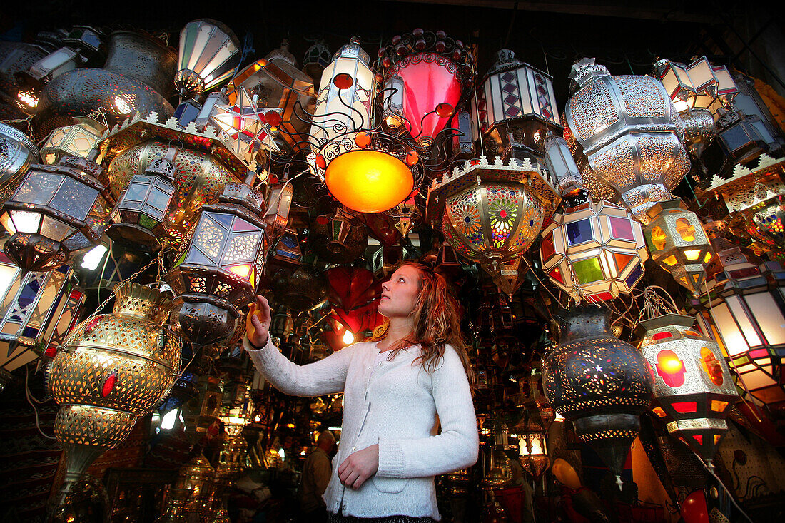 Young woman browsing for Moroccan lanterns in a market stall in the souk, Shopping in the Medina, Marrakesh, Morocco.