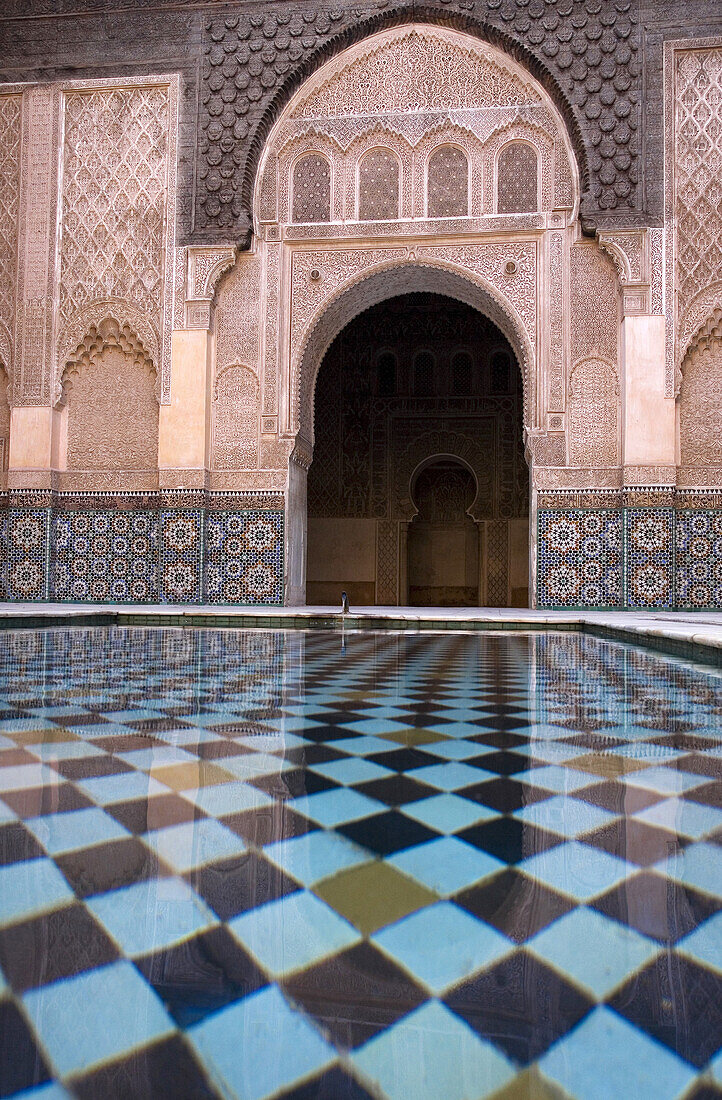 View across an ornamental pool at an arch in a courtyard at Ali Ben Youssef Medresa, Marrakesh, Morocco, Marrakesh, Morocco.