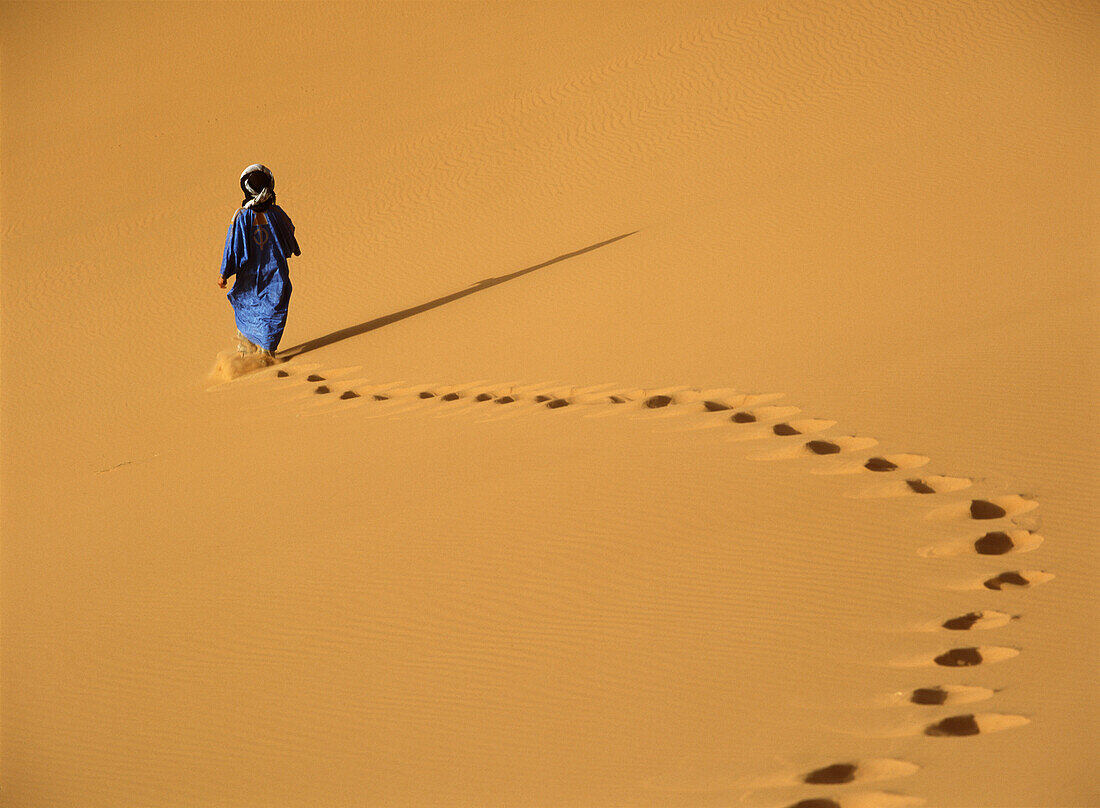 Berber walking across sand dunes in the Erg Chebbi area of the Sahara Desert, Merzouga, Morocco, Merzouga, Morocco.