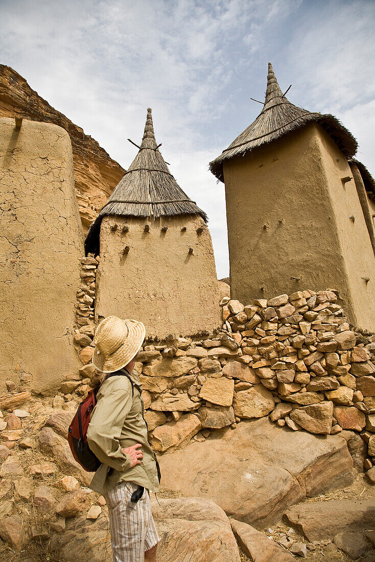 Tourist walking among Dogon village buildings, Bandiagara Escarpment, Dogon Country, Mali