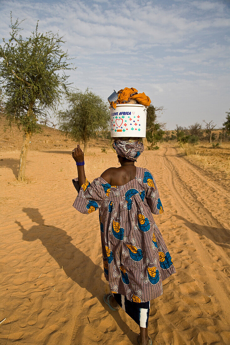 Woman walking with bucket on head at Bandiagara Escarpment, Dogon Country, Mali