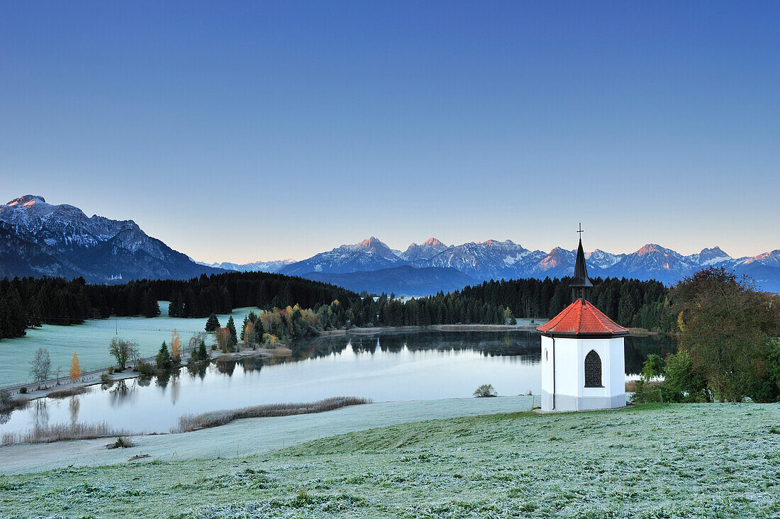 Chapel and lake with view to Ammergauer range and Tannheimer range at sunrise, lake Forggensee, Allgaeu, Allgaeu range, Swabia, Bavaria, Germany, Europe