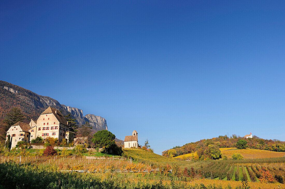 Manor house and church in vineyards in autumn colours with rockface in background, near lake Kalterer See, South Tyrol, Italy, Europe