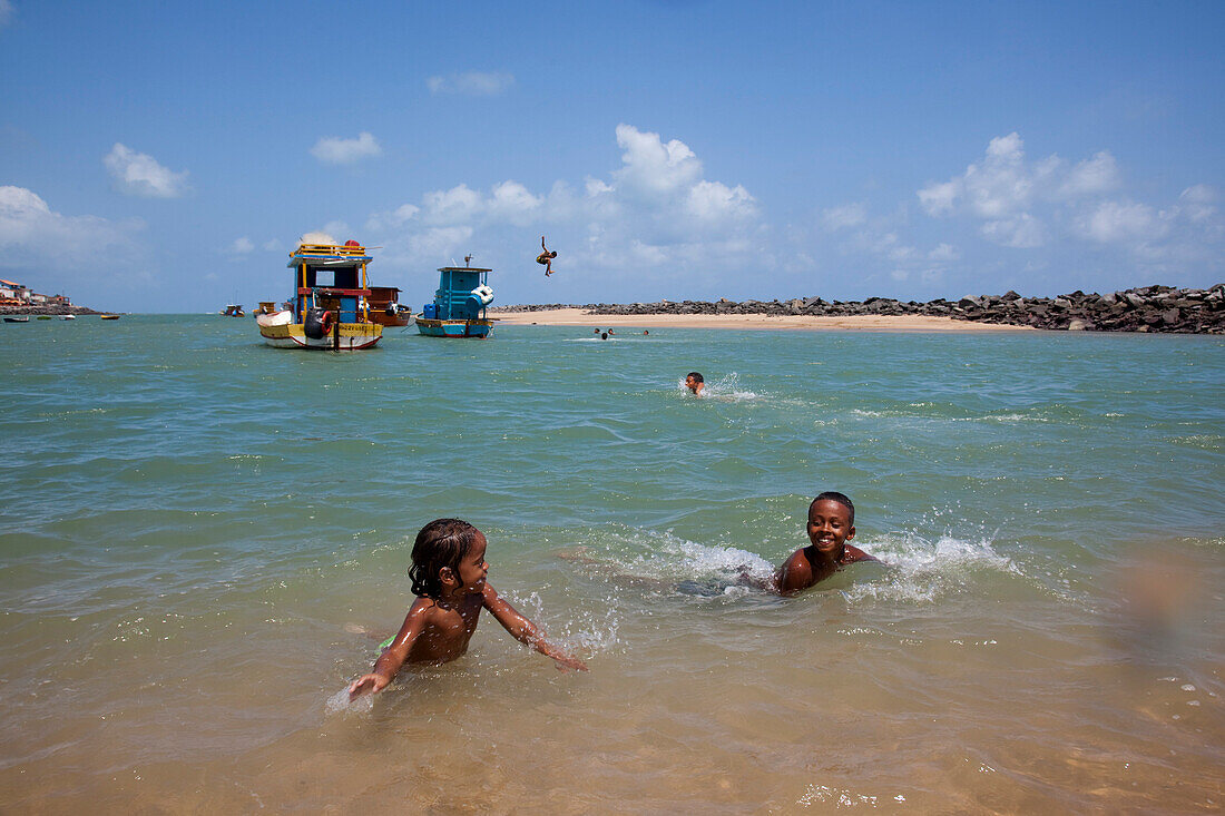 Children play in water at Olinda beach with teenagers jumping from fishing boats, Olinda, near Recife, Pernambuco, Brazil, South America