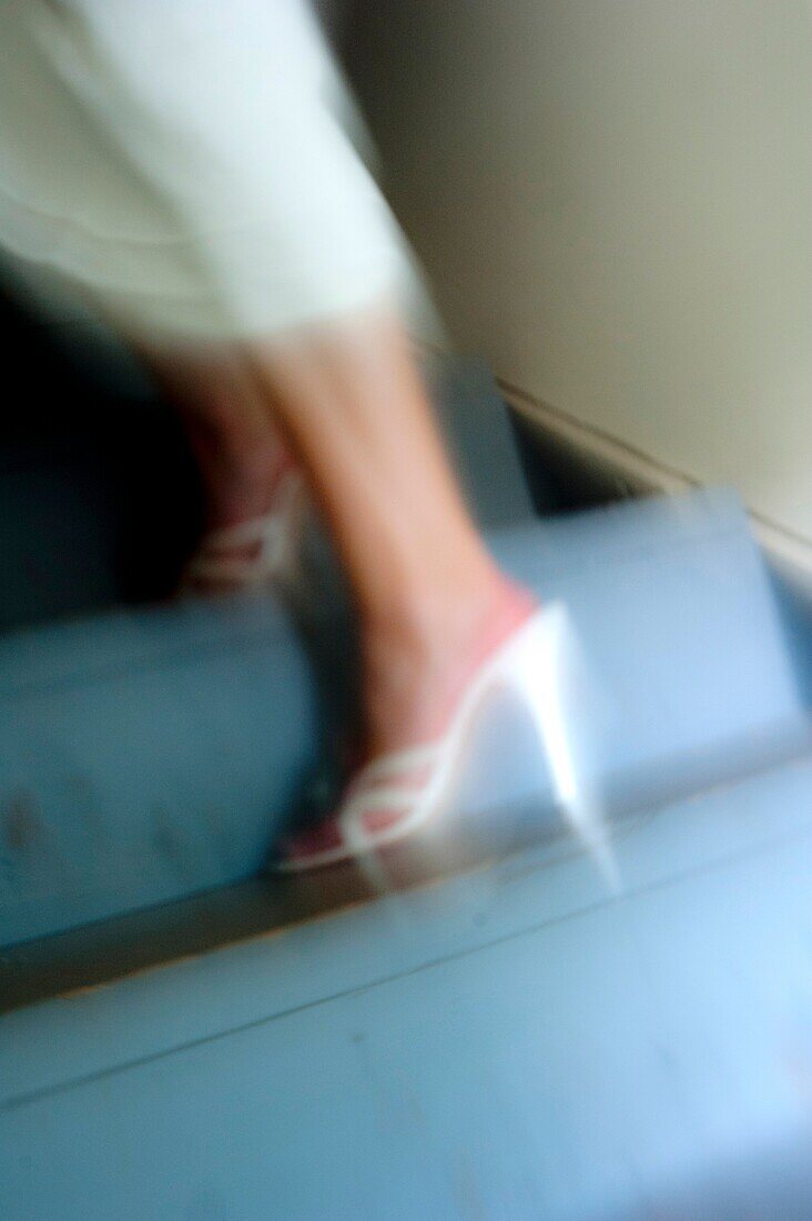 Blurry woman´s legs in heels and white dress on a stair way