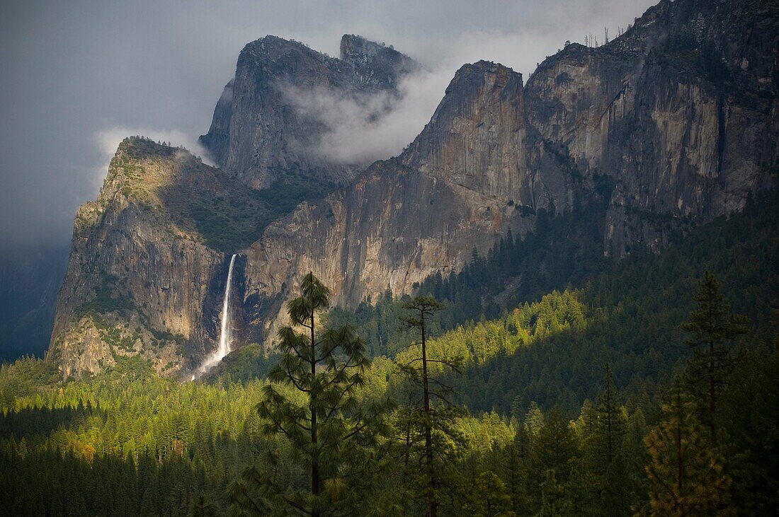 Sunlight and storm clouds over Bridalveil Fall waterfall and forest, Yosemite Valley, Yosemite National Park, California