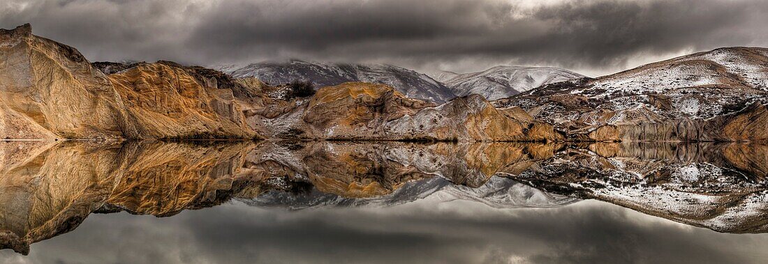 Blue Lake reflections of clay cliffs after winter storm and snowfall, St Bathans, Central Otago, New Zealand.
