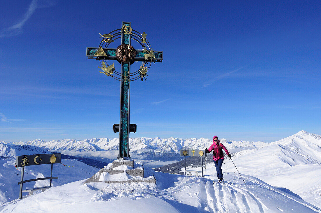 Woman backcountry skiing in front of a cross on the summit of Kleiner Gilfert, Tuxer mountain range, Tyrol, Austria