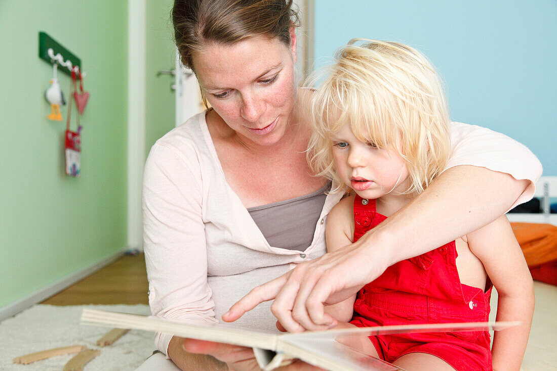Mother and daughter reading a book in the nursery, two year old girl, MR, Bad Oeynhausen, North Rhine-Westphalia, Germany