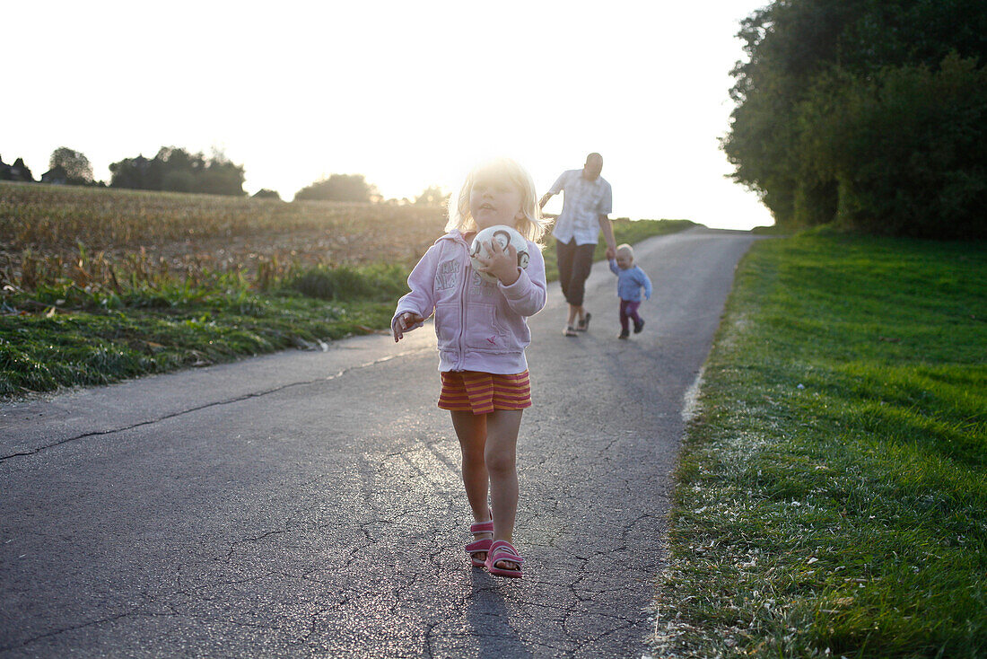 Kinder laufen auf einer kleinen Straße am Feldesrand im Abendlicht, MR, Bad Oeynhausen, Nordrhein-Westfalen, Deutschland