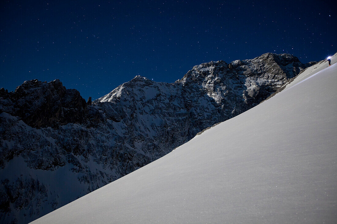 Person backcountry skiing in the moonlight with a headlamp, Alpspitz, Wetterstein, Alps, Bavaria, Germany