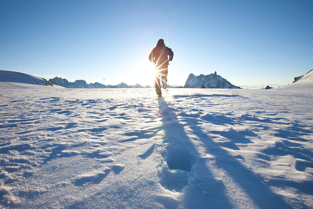 Man running over glacier towards sunrise, overlooking Les Grandes Jorasses and Dent du Geant, Chamonix Mont Blanc, France, Europe
