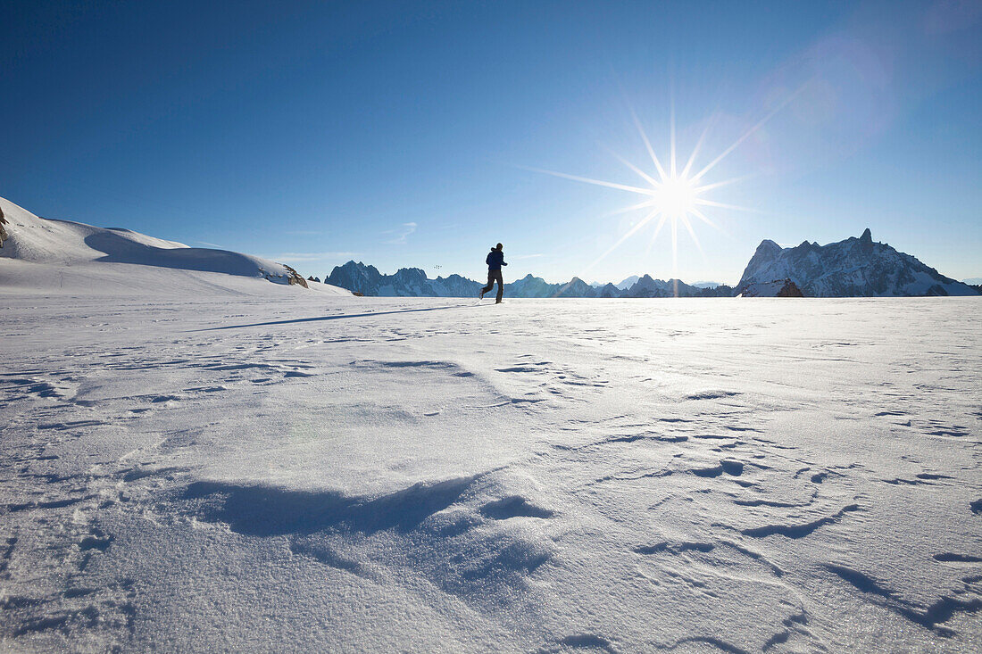 Man running over glacier towards sunrise, overlooking Les Grandes Jorasses and Dent du Geant, Chamonix Mont Blanc, France, Europe